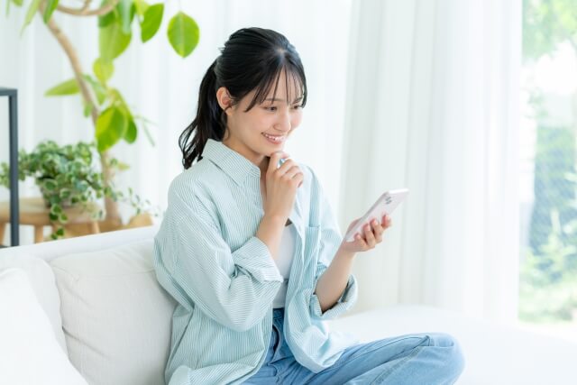 ソファでスマートフォンを操作する若い女性